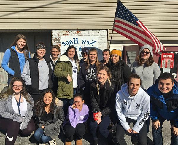 Group of students posing under flag at New Hope Shelter